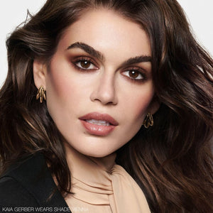 תמונת ביוטי של הדוגמנית KAIA GERBER עם איפור מלא, הכולל בסיס אחיד, סומק עדין, שפתיים בגוון טבעי ועיניים מודגשות בצלליות חומות. בתחתית התמונה מופיע טקסט המציין כי היא לובשת את הגוון VIENNA.