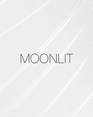 מריחה של סטיק הארה רב-שימושי Light Reflecting Luminizing Stick של NARS בגוון Moonlit, על רקע בהיר. התמונה מדגישה את הפורמולה השקופה ואת הגימור הזוהר והקורן של המוצר.