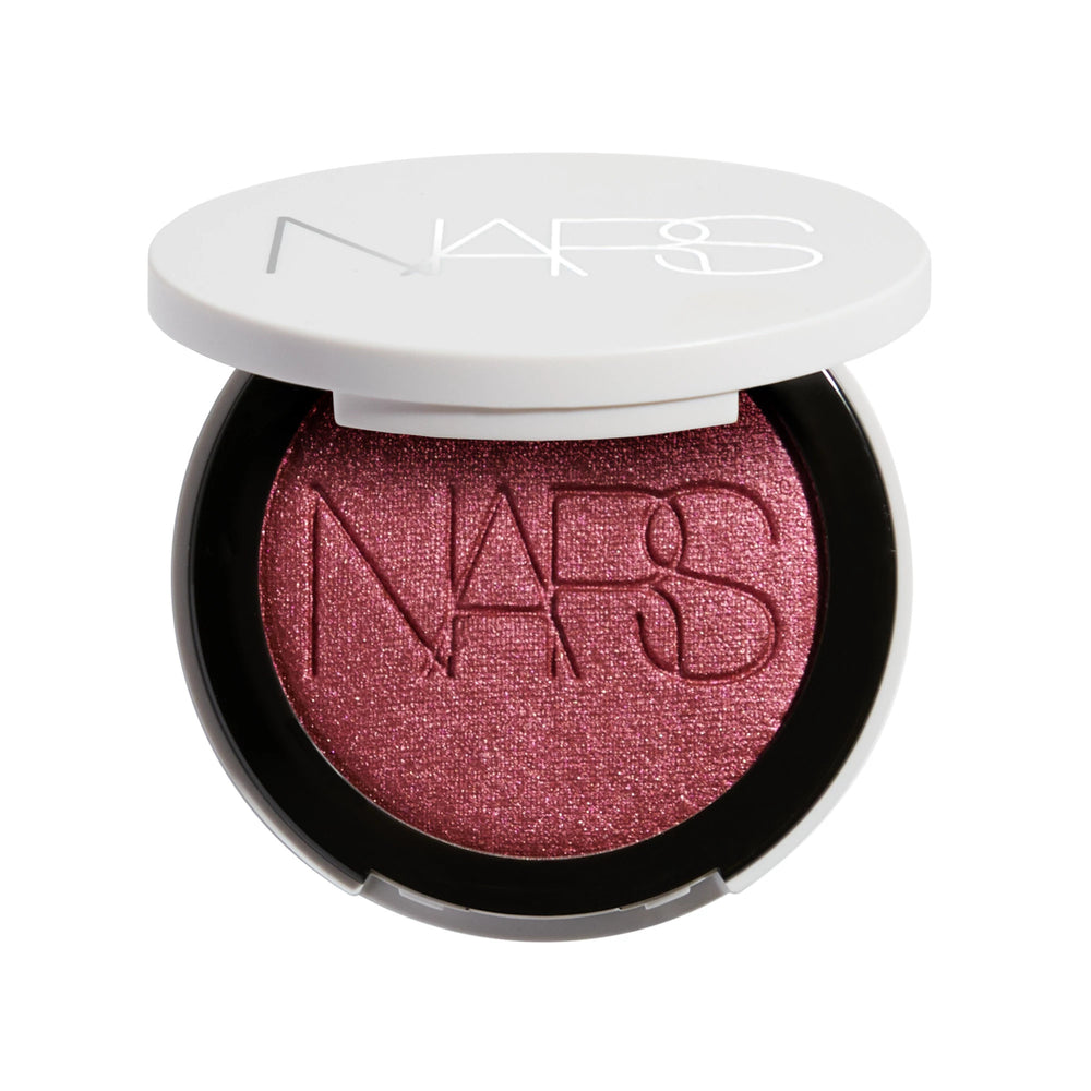 סומק פנינתי Light Reflecting Luminizing Blush של NARS, מוצג פתוח באריזה לבנה עגולה. הסומק בגוון ורוד-שזיפי עם גימור פנינתי וזוהר, המעניק ללחיים צבע עדין, ברק טבעי ומראה קורן.