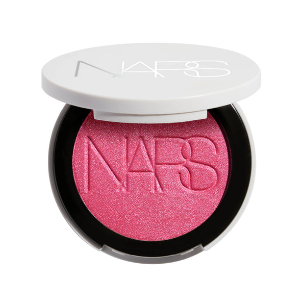 סומק פנינתי Light Reflecting Luminizing Blush של NARS, מוצג פתוח באריזה לבנה עגולה. הסומק בגוון ורוד פוקסיה עם גימור פנינתי וזוהר, המעניק ללחיים צבע חי, ברק טבעי ומראה קורן.