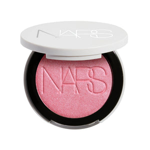 סומק פנינתי Light Reflecting Luminizing Blush של NARS, מוצג פתוח באריזה לבנה עגולה. הסומק בגוון ורוד בהיר עם גימור פנינתי וזוהר, המעניק ללחיים צבע עדין, הארה טבעית ומראה קורן.